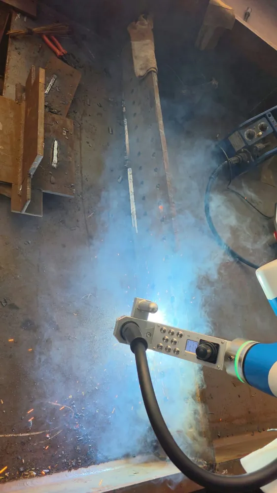 Cobot welding torch mid-arc inside a steel channel